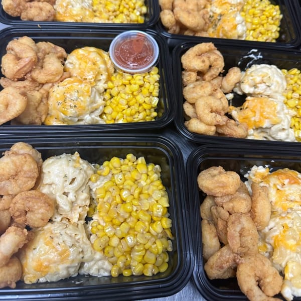 Multiple black takeout containers filled with fried shrimp, macaroni and cheese, and corn.
