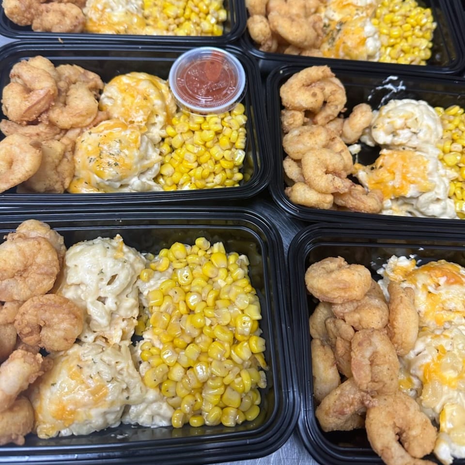 Multiple black takeout containers filled with fried shrimp, macaroni and cheese, and corn.