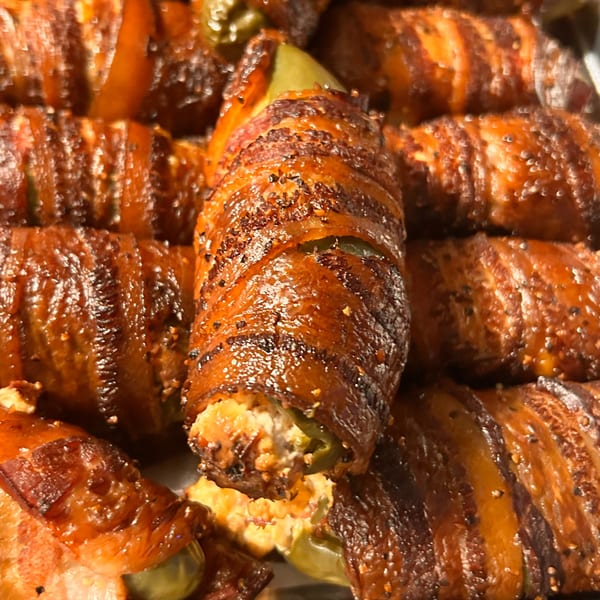 Close-up of several bacon-wrapped jalapeño poppers, with one cut open to show the creamy filling.