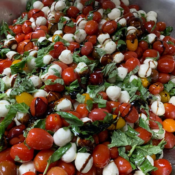 Close-up of a Caprese salad with cherry tomatoes, mozzarella balls, basil, and balsamic glaze.